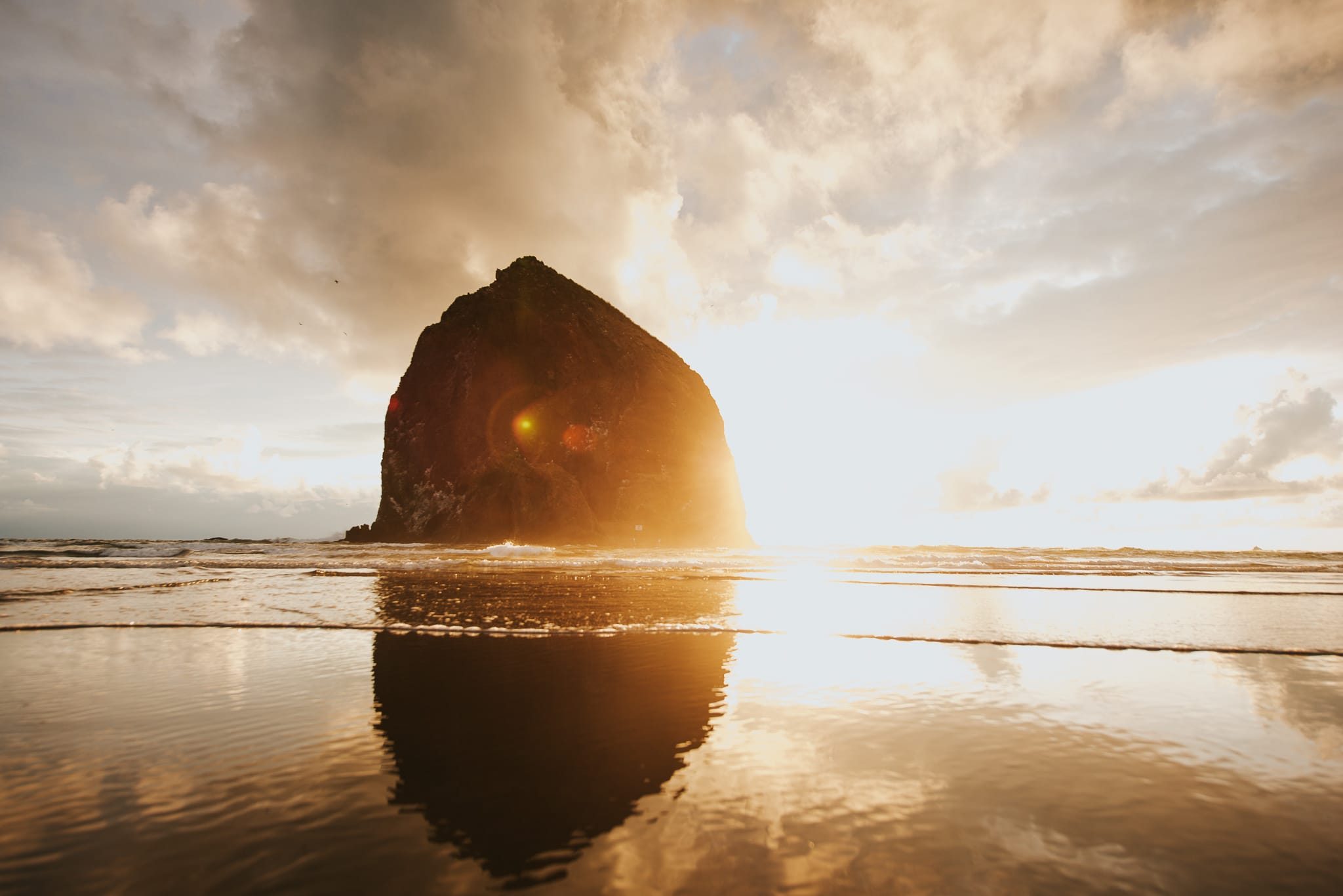 Haystack Rock silhouetted against the setting sun and reflected in the wet sand at Cannon Beach, Oregon